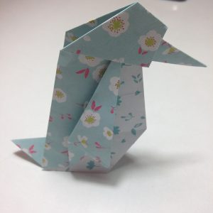 Nokkaansa riiputtava paperista taiteltu origami katsoo oikealle.